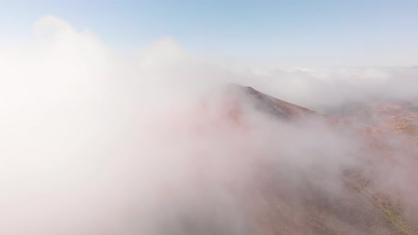 Drone Flying Through Clouds and Fog Above Mountain Peak