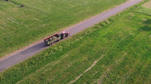 Tractor Carries a Trailer with Hay Through the Countryside alt