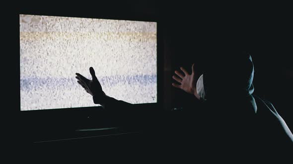 Silhouette Man in Hood and Medical Mask Watching TV Interference with Hands Up alt
