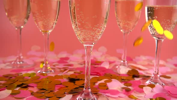 Falling confetti on the background of glasses with sparkling wine on a pink background. Slow motion. alt
