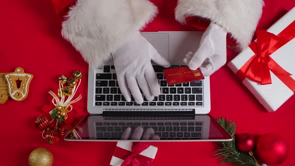 Top View Santa Hands in White Gloves Are Typing on the Keyboard By Red New Year Decorated Table alt