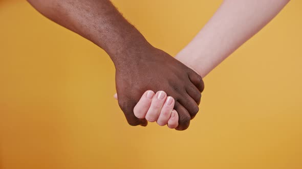 Black and White Hands Holding Together Isolated on the Orange Background. Close Up alt
