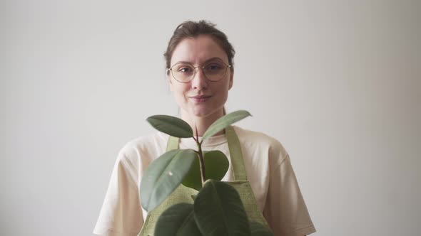 A Female Entrepreneur in an Apron Holds a Green Plant and Looks Into the Camera