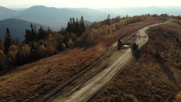 Quad bikes and SUV going on mountaint road. Sunny Autumn daytime. Aerial view. alt