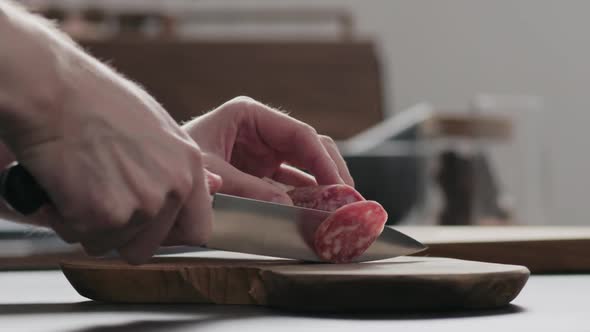 Slow Motion Man Slicing Salame on Olive Wood Board on Concrete Countertop
