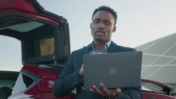 African American Man Holding Wireless Laptop While Leaning on His Luxury Red Car alt