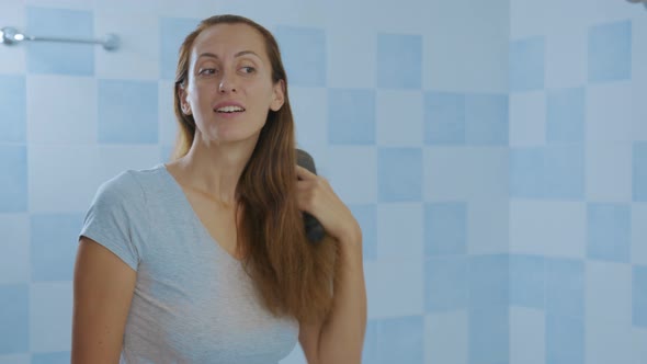 Woman Looking at Mirror, Brushing Hair. Irritated Young Girl Dissatisfied with Damaged Dry Hair alt