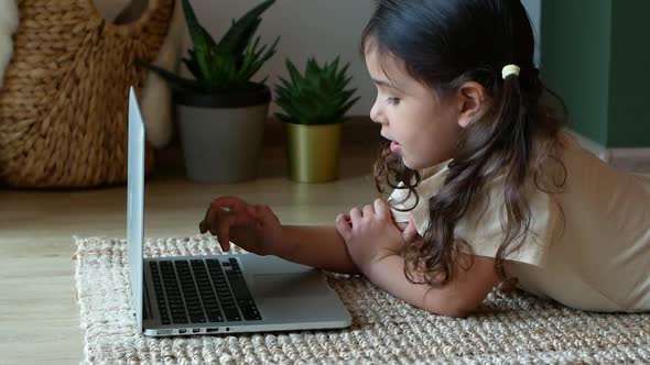 A little girl plays with her laptop sitting on the floor.