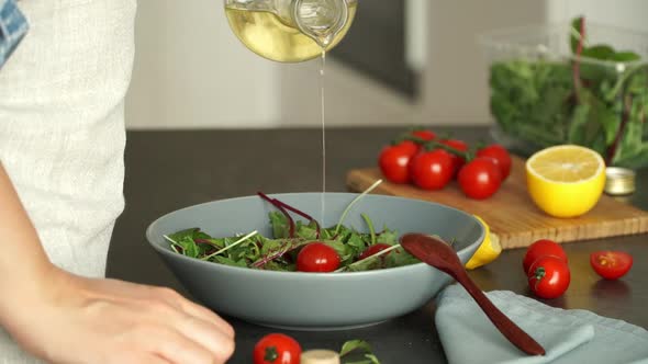 Hands Pour Olive Oil in Green Salad of Tomatoes and Fresh Lettuce Leaves Stir with Spoon