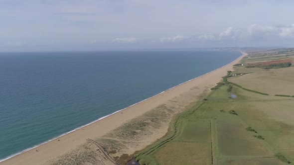 Aerial tracking forward high above Chesil Beach at Abbotsbury looking along the coastline to the wes alt
