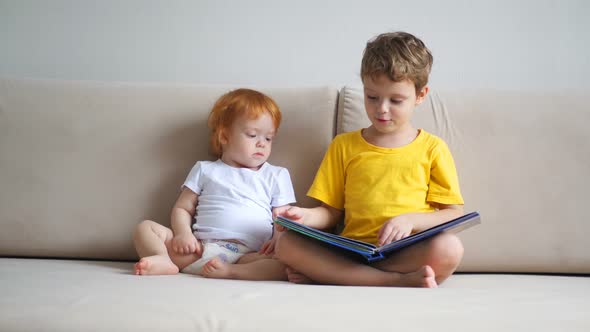 Brother and Sister Are Reading a Book on the Sofa