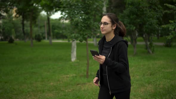 A Young Woman is Jogging with Her Phone in the Park alt
