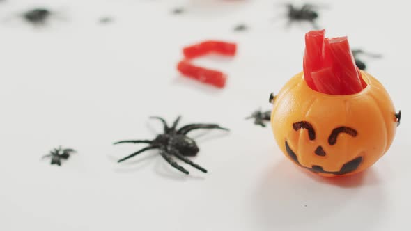 Candies in scary halloween pumpkin printed bucket and spiders toys against grey background alt