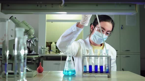 Scientist in Laboratory Doing Chemical Experiment with Blue Liquid in Test Tubes alt