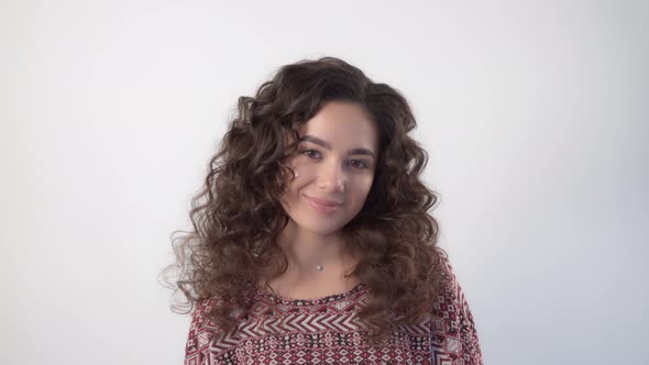 A young woman with long curly hair looks at the camera with a slight smile alt