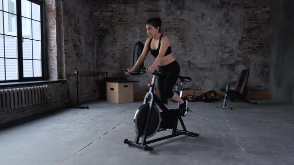 Young Athletic Indian Woman Doing a Workout, Engaged in Cycling Dressed in Sportswear Black alt