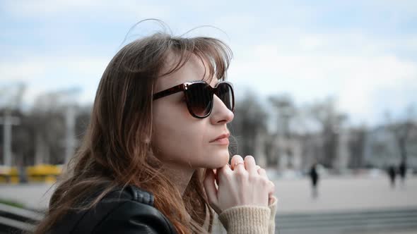 Side View of a Young Sad Girl Portrait in Sunglasses Sits on the Street of Her City and Yearns alt