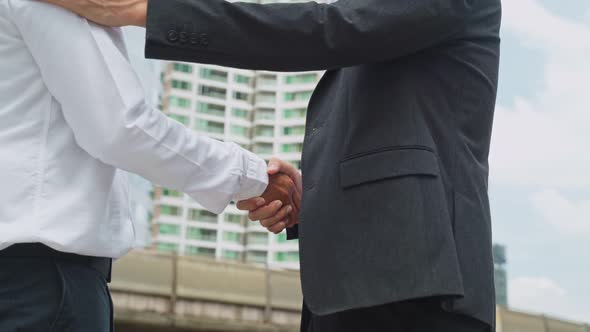 Close up shot, Asian business men partnership making handshake in the city building in background. alt