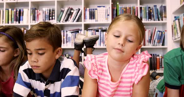 Teacher and kids lying on floor reading book in library alt