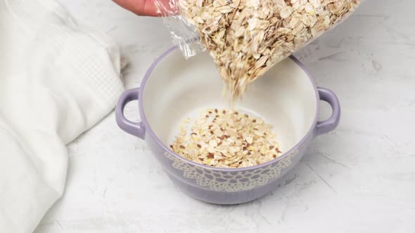 a woman's hand pours oatmeal from a transparent plastic bag into a round ceramic plate alt