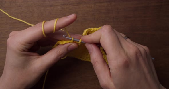 Close up top shot of caucasian hands doing some needle work: crochet. Yellow wool laying on the tabl alt