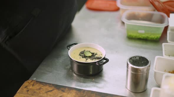 Close Up of Chef Hand Adding a Leaf To a Cream Soup alt