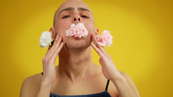 Closeup Portrait of Queer Person Holding Flowers in Mouth and Hands Posing at Yellow Background alt