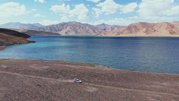 Aerial on Side of Off Road 4X4 Car Driving Along Gravel Trail Path Toward Lake in Arid Mountains alt