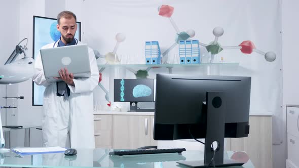 Doctor in His Modern Office Standing and Typing at His Laptop alt
