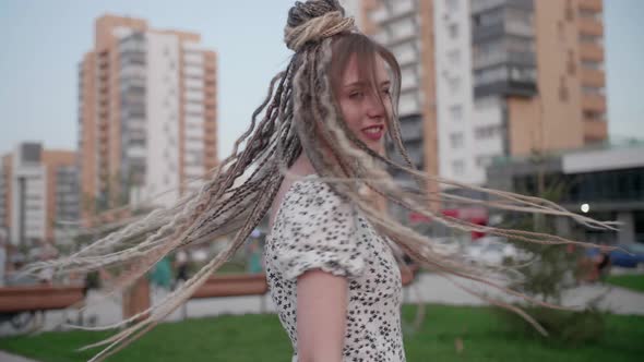 A Cute Young and Happy Girl with Dreadlocks Walks Down the Street and Poses