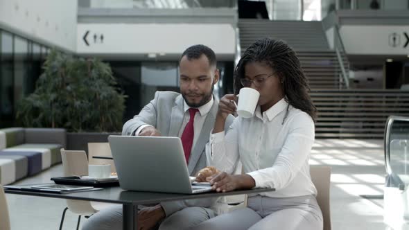 Slow Motion Shot of Two Colleagues with Laptop Sitting at Cafe alt