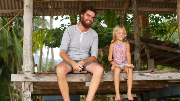 Dad and Daughter are Sitting on the Bridge Near the Sea alt