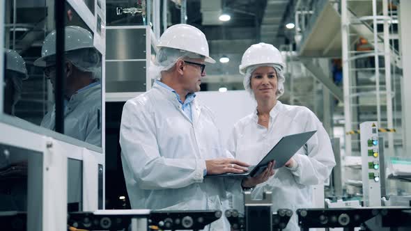 Factory Specialists are Smiling While Talking Next to the Conveyor alt