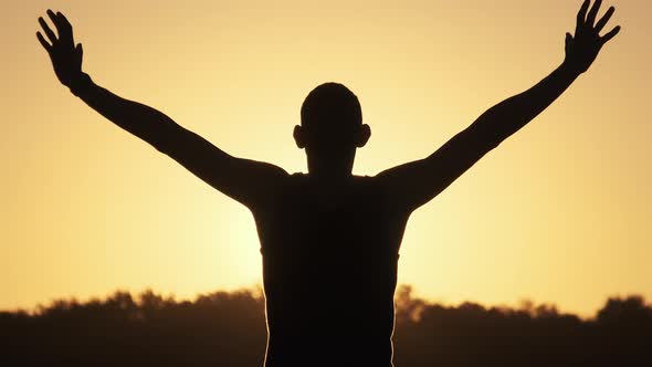Silhouette of Young Man Against Sunset Raising Hands Sides and Up. Slow Motion alt