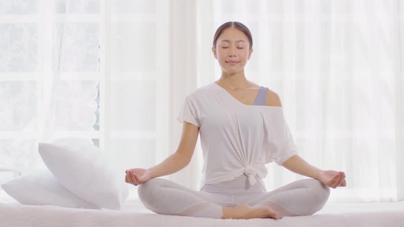 Calm of wellness Asian young woman sit on bed breathing with yoga lotus pose alt