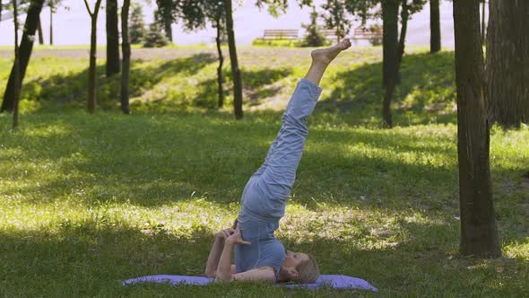 Senior Fit Woman Doing Yoga in Park on Mat, Shoulder Stand Asana, Slow-Mo alt