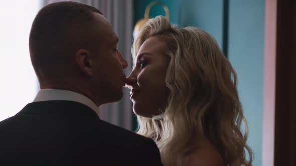Bridegroom Kisses Nose of Beloved Woman in Hotel Room alt