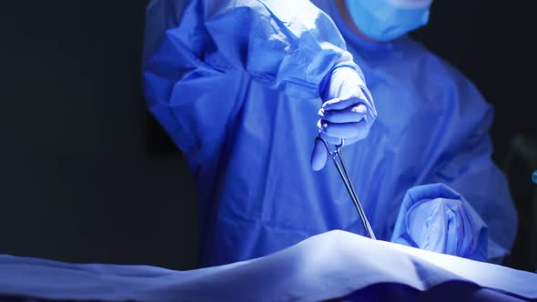 Mid section of surgeon wearing protective clothing holding scissors in operating theatre alt