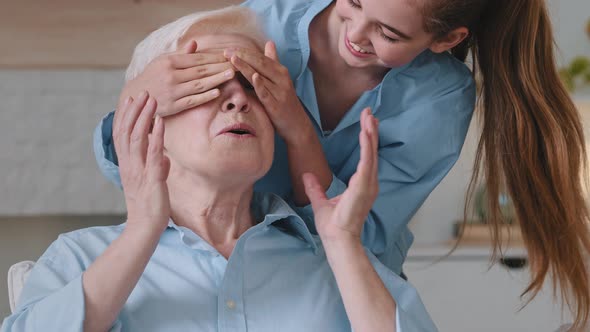 Little Granddaughter Making Surprise Hugging Happy Old Grandmother Closing Eyes with Palms Smiling alt