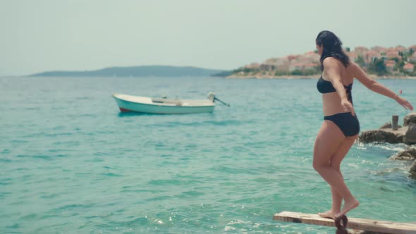 The Girl Jumps Into the Water From the Pier By the Sea alt