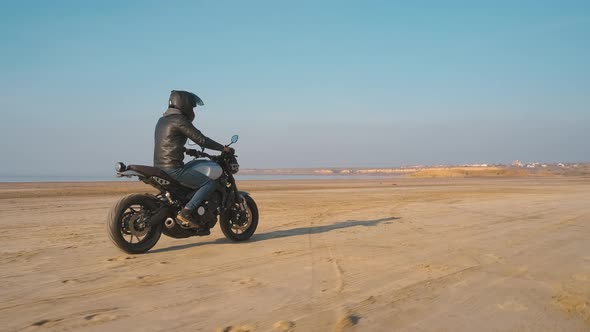 Motorcyclist Driving His Customized Fast Motorbike on the Dirt Road in Desert Around Sea or Lake alt