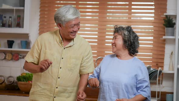 Asian senior couple dancing and cooking in the kitchen at home.