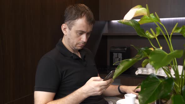 Man with Phone Sits in a Restaurant with Cup of Coffee and Reading Bad News alt