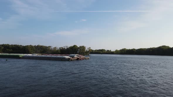 Empty barges being pushed up the Mississippi River on a bright summer day. Trees on islands.