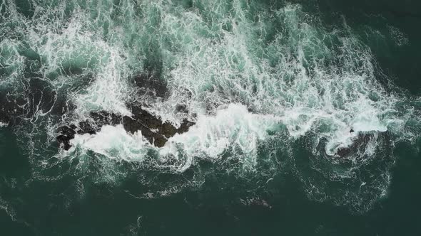 Aerial top down view of waves splashing into rocks in the sea, super slow mot