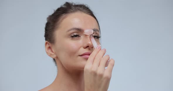 Beautiful Woman Using Stone Facial Roller Over Gray Background alt