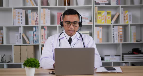 Doctor with headset making conference call on laptop alt