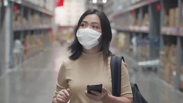 Asian woman wearing mask walking in warehouse and use smart phone.