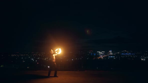 Young Blond Male Plays with Two Fire Torches Spins Them at Night on Black Background alt
