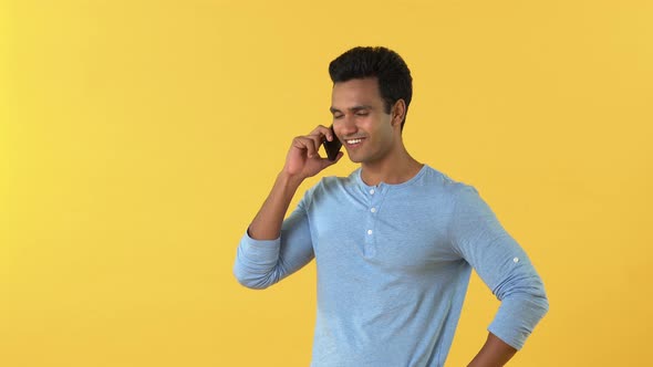 Young smiling Indian man talking on cell phone isolated on yellow studio background